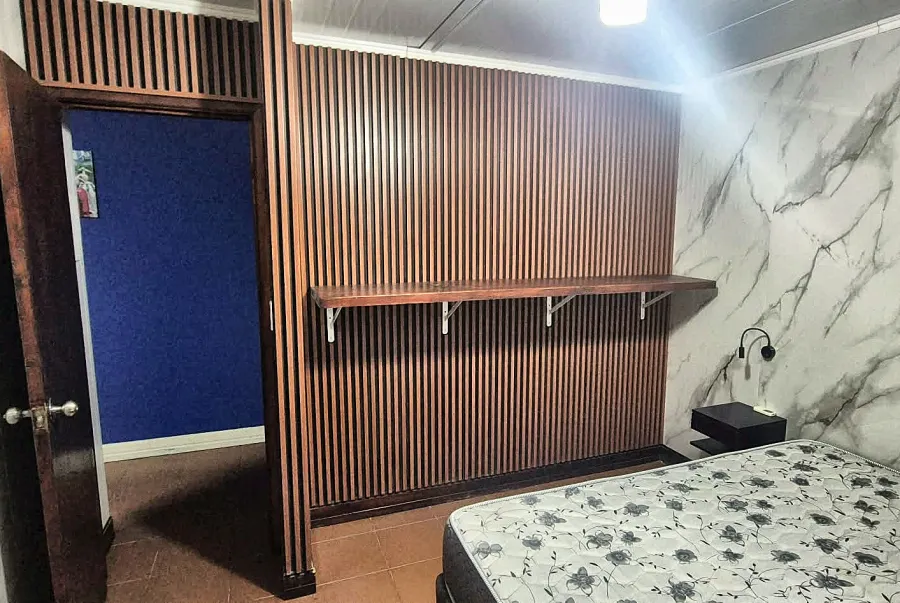 Dormitorio con cama matrimonial, paredes símil mármol y estante de madera